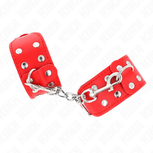 Paire de manchettes rouges à rivets et anneaux en D reliées par une chaîne, vue rapprochée des boucles, accessoire de contention BDSM au look affirmé.