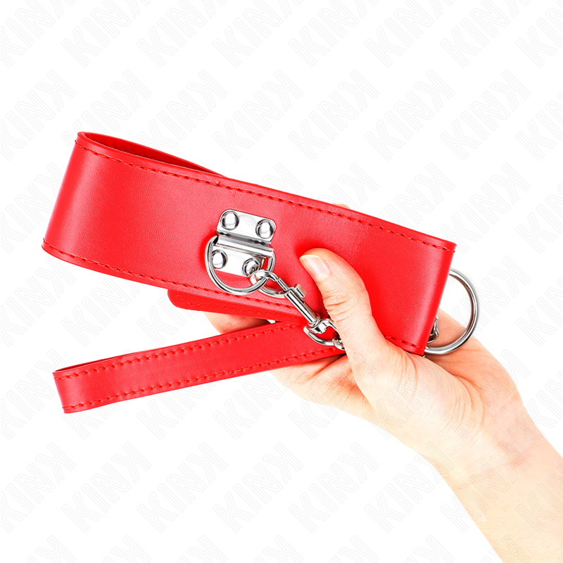 Collier large rouge à anneau en D tenu en main, gros plan sur la boucle métallique et la sangle, accessoire de soumission BDSM coloré et solide.