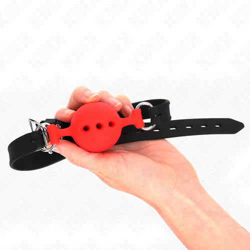Baillon boule rouge silicone tenu en main, boule a trous et longue sangle noire reglable, version coloree du classique du jeu de domination