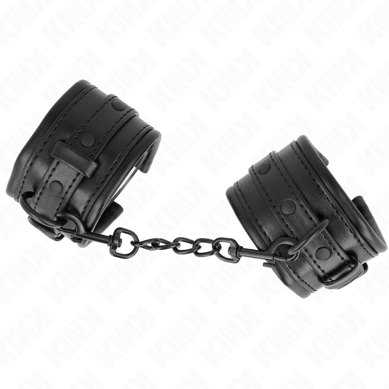 Gros plan de menottes de poignets en cuir noir a rivets reliees par une chaine sombre : accessoire de contention BDSM robuste pour le jeu de domination a deux.