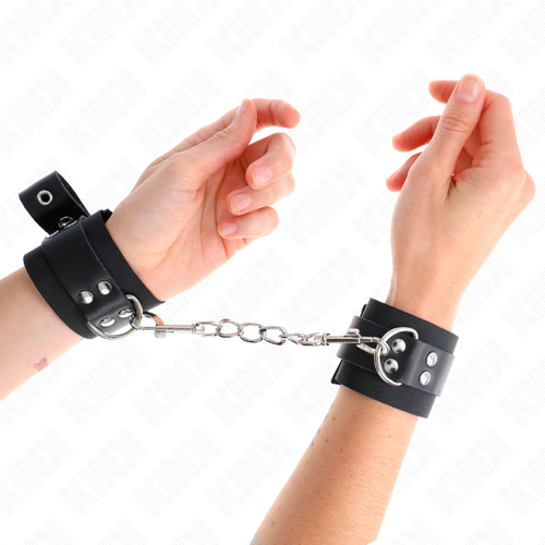 Poignets entravés par des menottes en cuir noir à boucle reliées par une chaîne argentée, anneau pivotant visible, kit d'attache de bondage pour la soumission