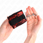 Manchette de poignet noire a motif dentelle rouge et mousqueton tenue en main, format ajustable pour des jeux d'attache doux et sensuels.