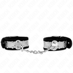Paire de manchettes de poignets noires a large plaque argentee cloutee reliees par chaine, posees sur fond blanc, accessoire de soumission glamour.