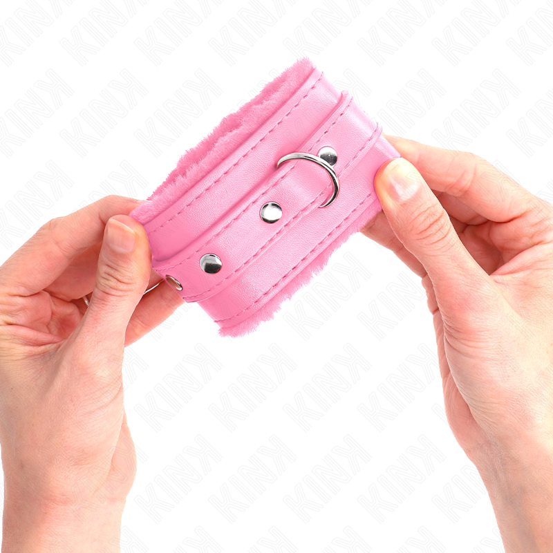 Menotte de poignet rose pastel bordee de fourrure tenue des deux mains, rivet visible : accessoire de contention moelleux et feminin pour les jeux de soumission.
