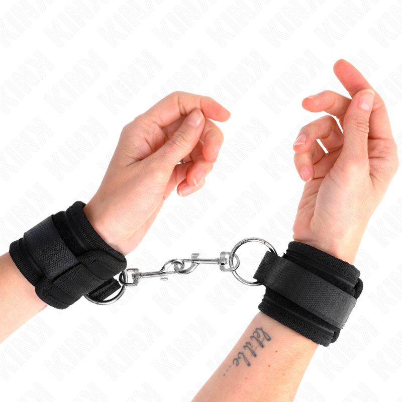 Manchettes de poignet en simili noir reliées par une chaîne, portées sur deux poignets croisés, vue rapprochée, contention ajustable de 35 cm pour le bondage.