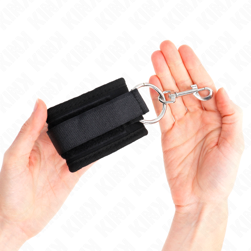 Manchette en nylon noir tenue dans une paume, gros plan sur le crochet mousqueton d'attache, attache-poignet réglable pour découvrir la domination en douceur.