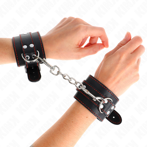 Poignets entravés par des menottes en cuir noir à surpiqûres reliées par une chaîne, anneau pivotant visible, kit d'attache de bondage pour la soumission