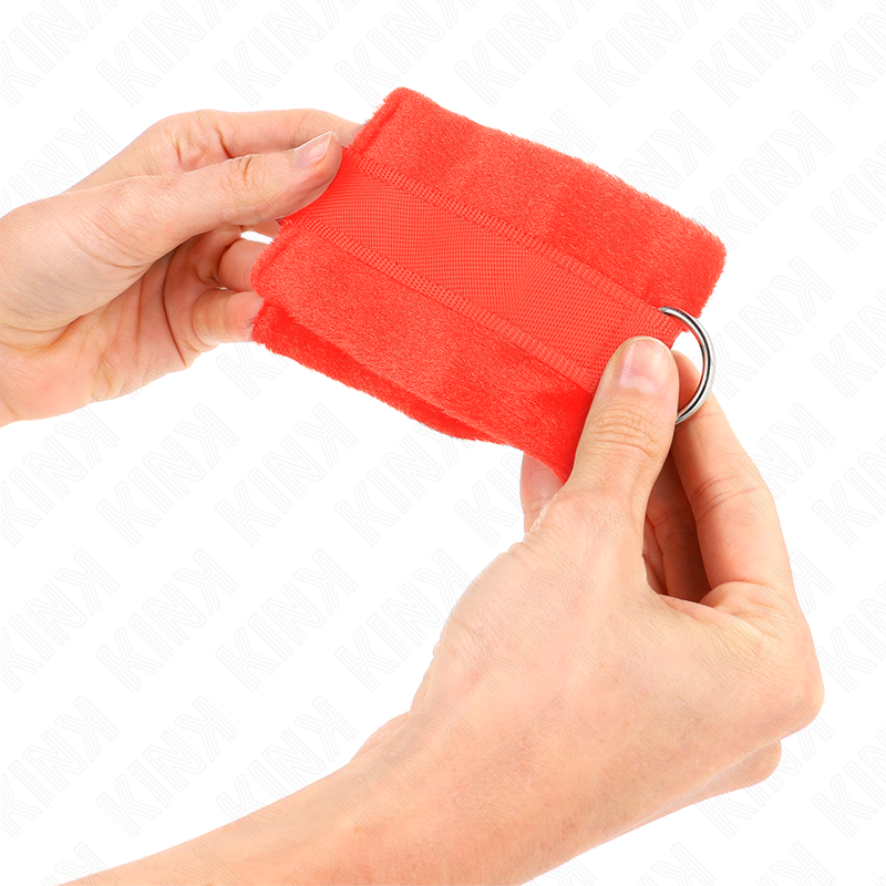 Manchette en fourrure rouge tenue à deux mains, gros plan sur l'anneau métallique et le velcro, attache-poignet moelleuse pour domination tout en douceur.
