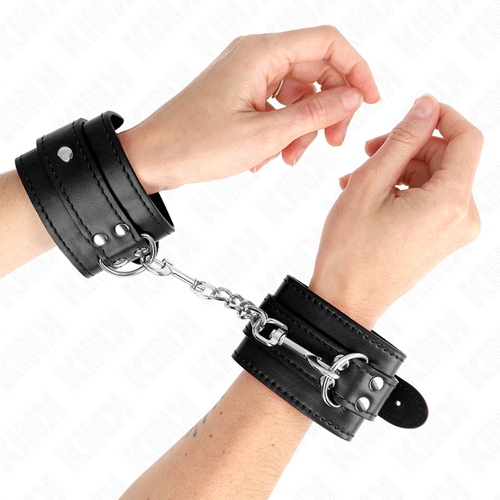 Poignets entravés par des menottes en cuir noir à boucle reliées par une chaîne métallique, kit d'attache de bondage au style sobre pour la soumission