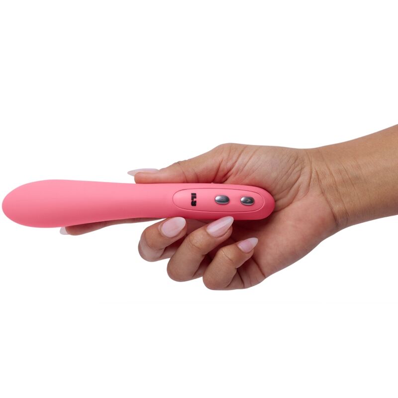Vibromasseur wand point G rose posé en travers d'une main ouverte, tige incurvée et boutons argentés visibles, plan montrant la longueur et la taille de l'objet lisse sur fond blanc.