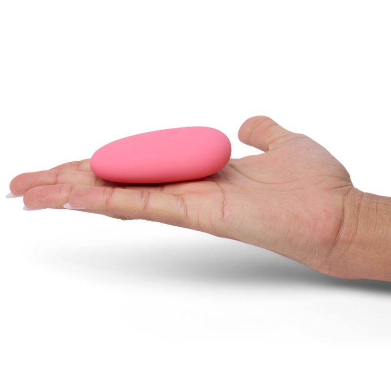 Mini galet clitoridien rose posé au creux d'une paume ouverte, petite forme lisse arrondie bien visible, plan illustrant la taille discrète et compacte du produit sur fond blanc épuré.