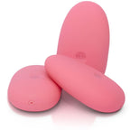 Trois galets clitoridiens roses lisses disposés sous différents angles, formes ovales bombées en silicone, mise en scène produit jouant sur les reflets sur fond blanc parfaitement épuré.