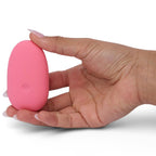 Galet clitoridien rose tenu du bout des doigts d'une main, forme ovale lisse vue de profil, plan présentant le format de poche et la discrétion du produit sur fond blanc épuré.