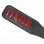 Paddle de fessée en cuir noir, gros plan sur le message XOXO rouge en relief, accessoire de discipline qui marque la peau pour le jeu de rôle dominant-soumis.