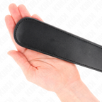 Paddle de fessee noir pose a plat dans une main ouverte, montrant sa surface souple et fine, accessoire de spanking maniable pour la discipline a deux.