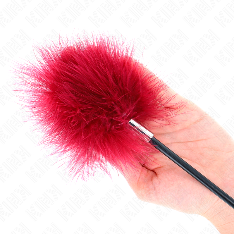 Gros plan du pompon de plumes rouges du plumeau cravache pres d'une main, marabout moelleux qui frole et fait frissonner la peau, jeu sensoriel.
