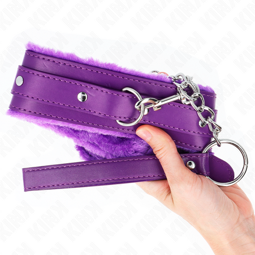 Collier de soumission en cuir violet doublure fourrure tenu dans une main, anneau en D et dragonne visibles, accessoire de jeu de soumission vif.