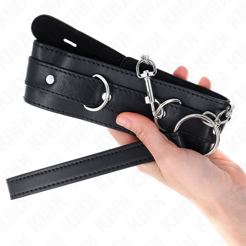 Collier de soumission noir matelassé tenu en main, gros plan sur les anneaux en D et la boucle, accessoire BDSM dominant-soumis confortable et solide.