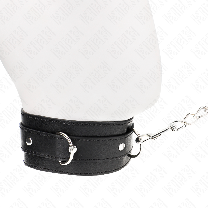 Collier noir à anneaux en D fermé autour du cou d'un mannequin, chaîne de laisse partant sur le côté, accessoire de soumission BDSM discret et ajustable.