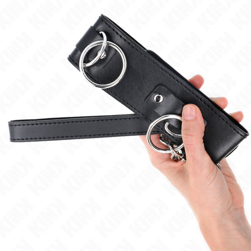 Collier de soumission noir à plusieurs anneaux argentés tenu en main, points d'attache bien visibles. Détail du collier BDSM modulable.
