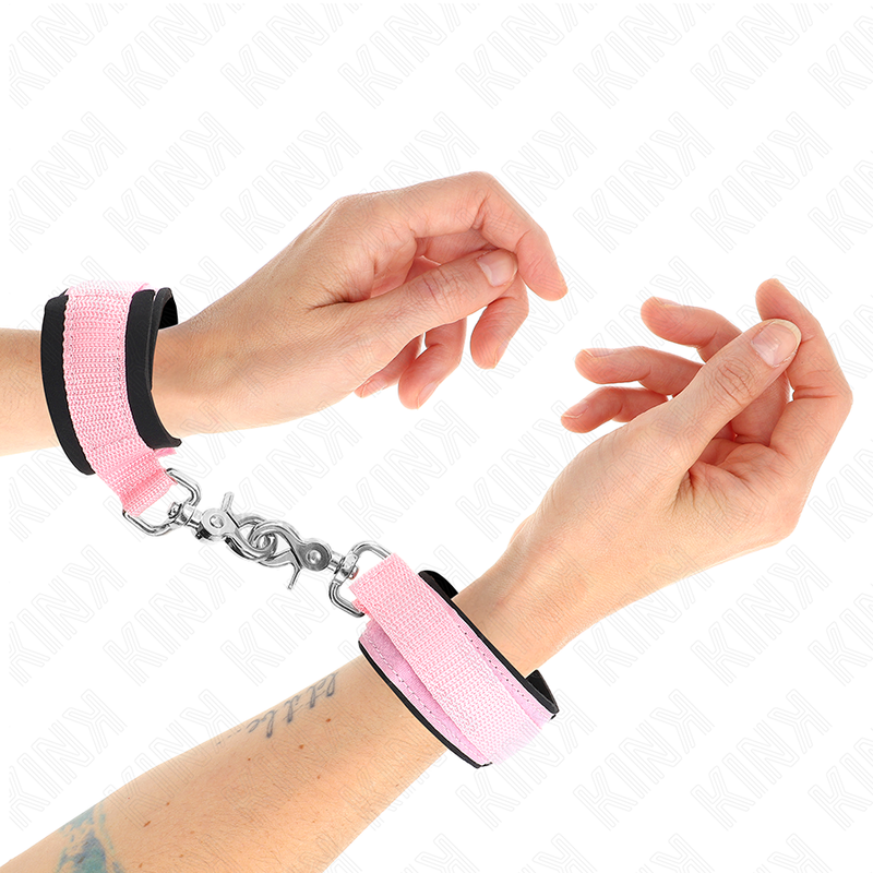 Manchettes de poignet en néoprène rose et noir portées avec mousqueton, gros plan sur le poignet, contention souple et réglable pour le bondage débutant.