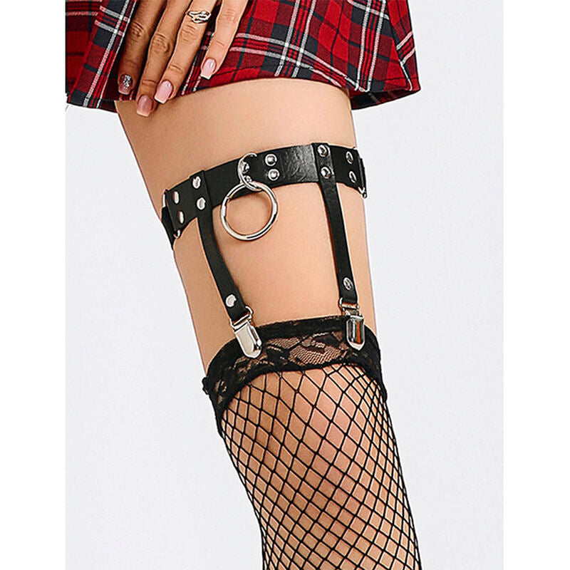 Harnais de cuisse cuir noir a anneau porte sur jambe nue avec bas resille, sangles cloutees Subblime sous une jupe a carreaux, accessoire fetichiste.