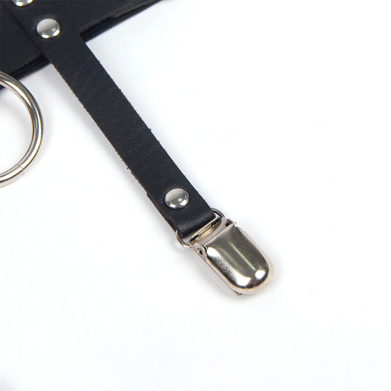 Gros plan de la pince metal jarretelle et de la sangle cuir noir cloutee du harnais de jambe Subblime, anneau visible, accessoire fetichiste pose a plat.