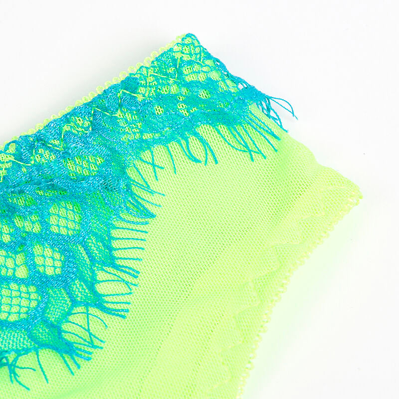 Macro sur la dentelle bleue a franges posee sur la maille vert fluo de la lingerie Subblime, texture florale et finition des bords mise en avant.