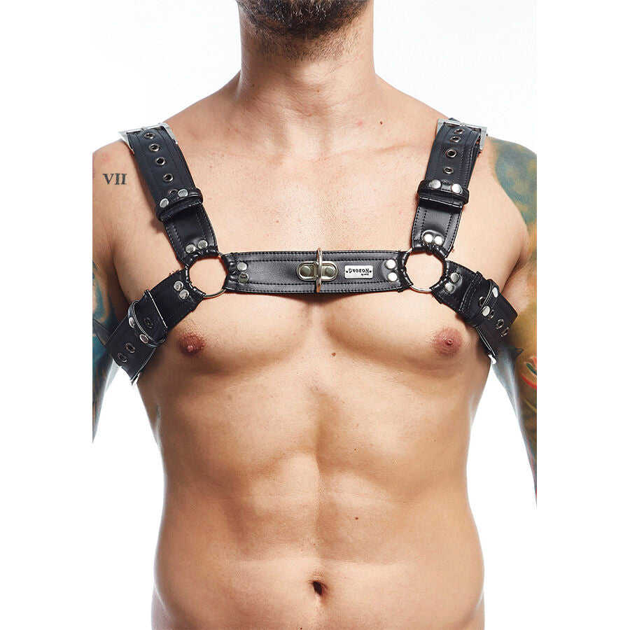 Harnais de corps homme en cuir a anneau central porte sur le buste, sangles structurantes et boucles metal, presente de face sur un torse masculin muscle.