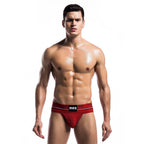 String homme rouge sur modele torse nu, vue frontale : pochette structuree a l'avant, coupe minimaliste extensible qui souligne la silhouette masculine avec audace.
