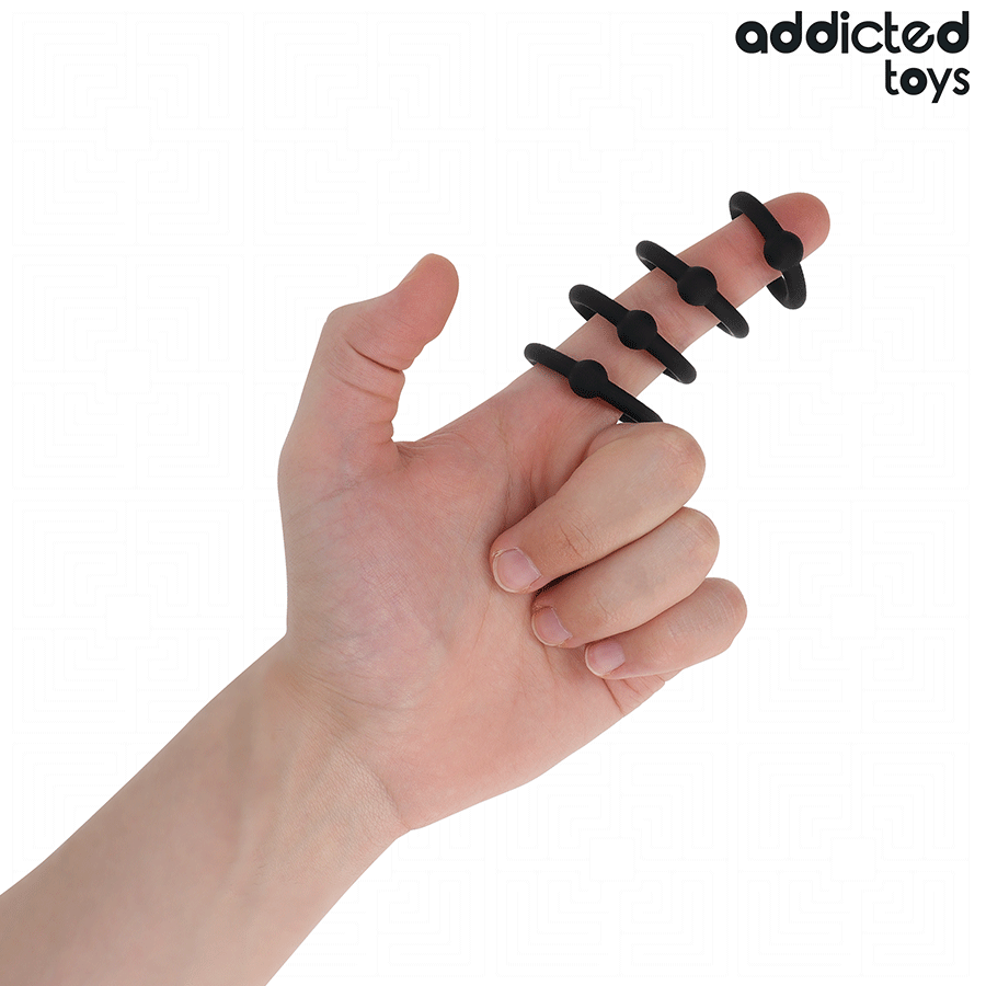 Quatre anneaux peniens a billes en silicone noir Addicted enfiles sur un doigt pour montrer leur pression, set de cockrings de maintien de l'erection.