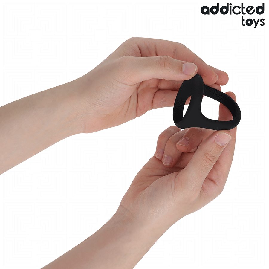 Anneau penien double en silicone noir Addicted tenu entre les doigts pour montrer ses deux boucles souples, cockring penis et testicules de maintien de l'erection.