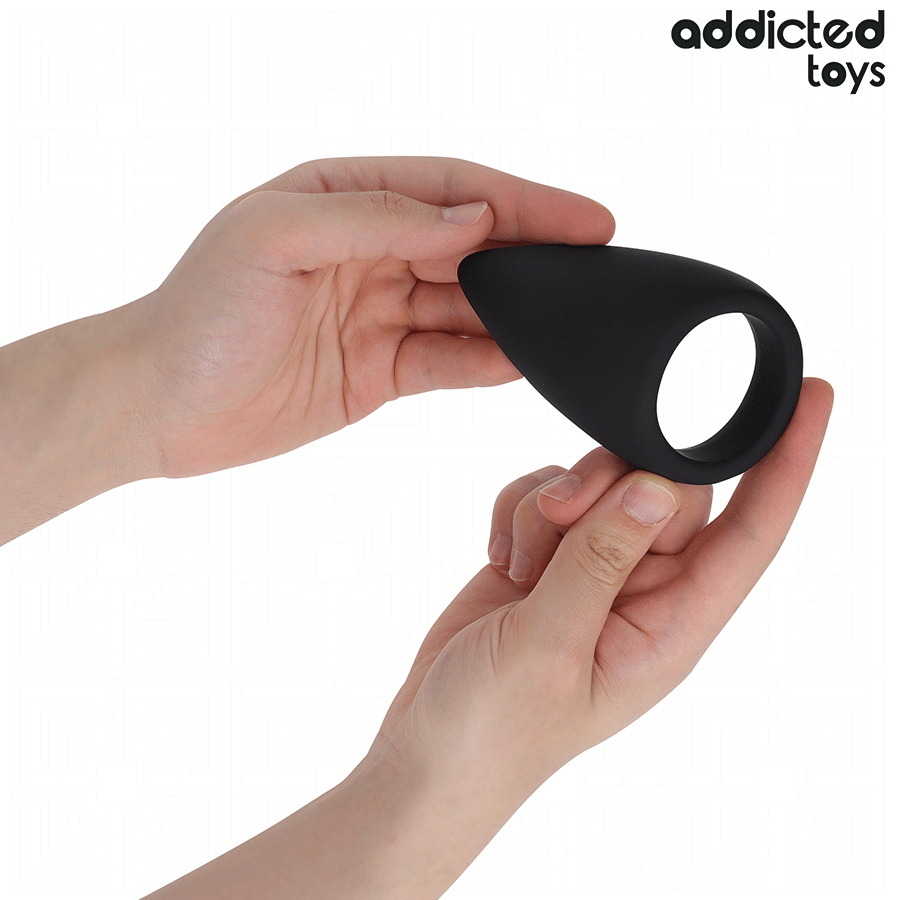 Anneau penien en forme de larme en silicone noir Addicted tenu entre les doigts pour montrer son galbe souple, cockring ergonomique de maintien de l'erection.