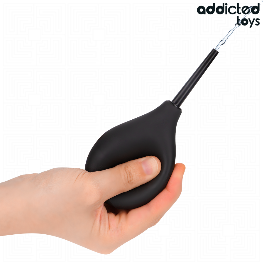 Poire de douche intime de voyage Addicted tenue en main, corps galbe en silicone noir et canule fine, montrant la prise en main confortable du nettoyeur.