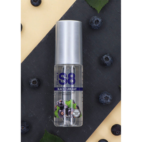 Flacon S8 Blackcurrant pose en biais sur fond noir et beige parseme de myrtilles, lubrifiant gourmand base eau saveur cassis, ambiance fruitee gourmande.