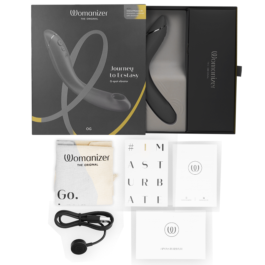 Boîte noire du Womanizer OG, câble de charge et cartes de notice à côté, stimulateur G-spot noir par ondes d'air, rechargeable. Présentation complète du coffret cadeau.