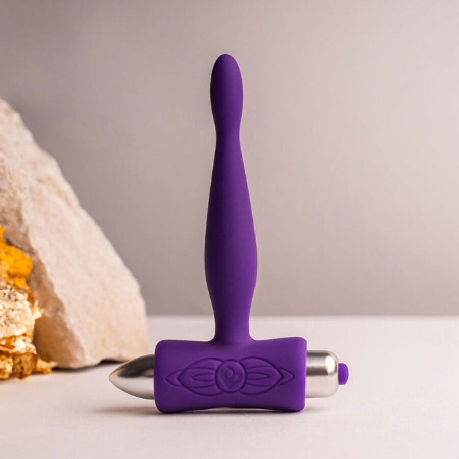Plug anal Teazer violet effilé dressé devant une pierre claire, tige souple silicone et base T ergonomique, stimulateur point P fin étanche signé Rocks-Off.