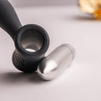 Très gros plan de la base T du plug anal Teazer noir avec sa balle vibrante argentée amovible posée à côté, détail du moteur de ce stimulateur point P silicone.