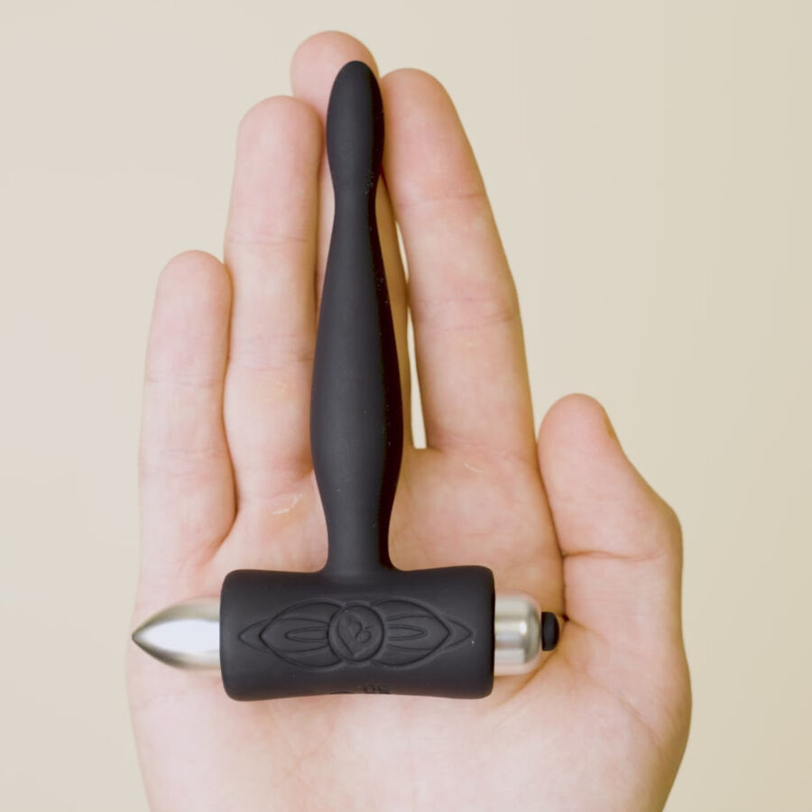 Plug anal Teazer noir posé sur les doigts d'une main, balle vibrante argentée visible sous la base T, illustrant la finesse de ce stimulateur point P silicone.