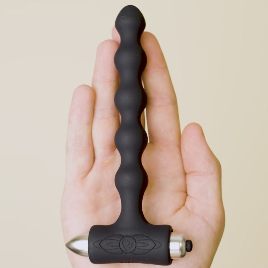 Plug anal perlé noir tenu contre une paume ouverte illustrant sa longueur, chapelet de billes progressives et base en T visibles, silicone lisse sur fond beige.