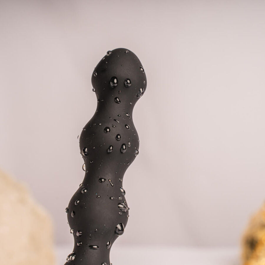 Macro du chapelet de billes noires du plug couvert de gouttes d'eau, renflements étagés lisses entre deux pierres claires, illustrant l'étanchéité de l'accessoire.