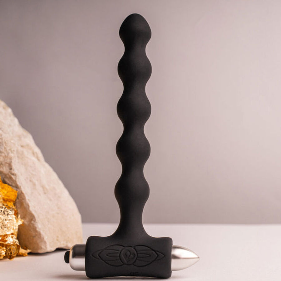 Plug anal perlé noir dressé devant une pierre claire et un éclat doré, chapelet de billes étagées et base en T lisses, silicone mat présenté sur fond neutre sobre.