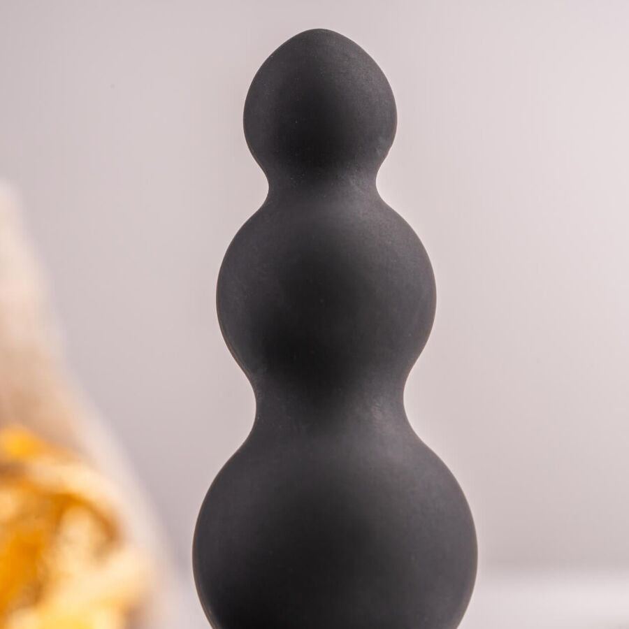 Gros plan des billes progressives noires du plug anal sur fond flouté, renflements lisses étagés et col fin mis en valeur, silicone mat sans relief figuratif.
