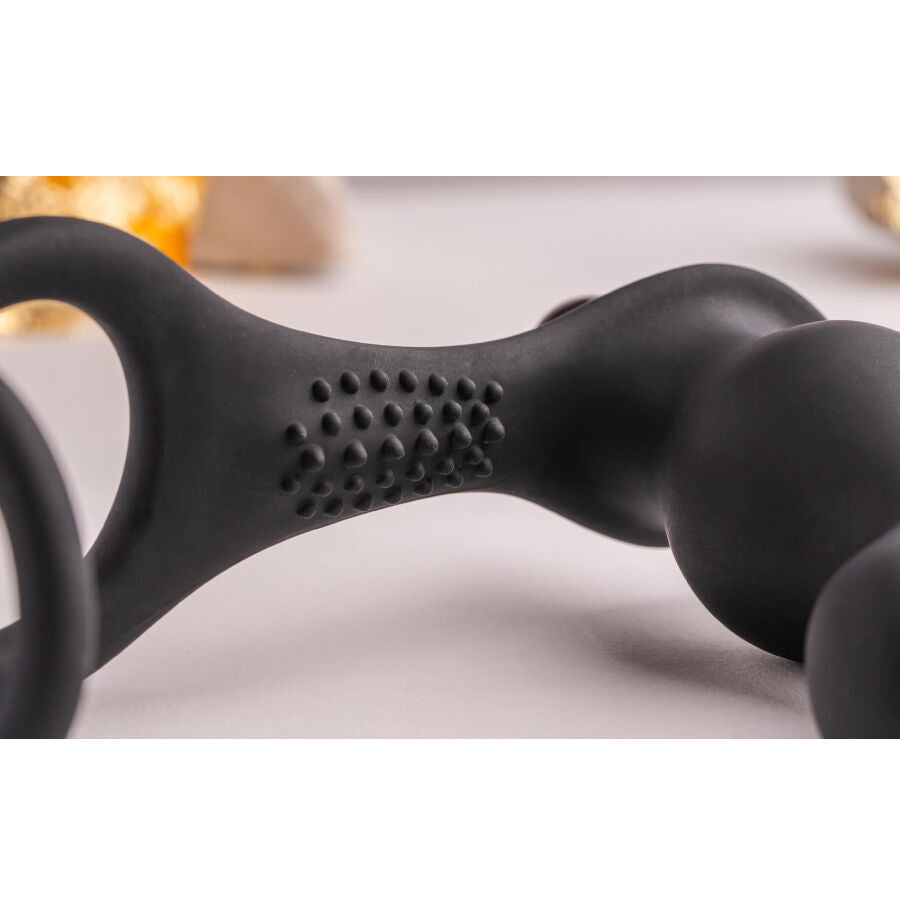 Macro de la partie texturée à picots du combiné plug-anneau noir près d'un éclat doré, tige courbe et reliefs en silicone lisse mis en valeur sur fond clair.