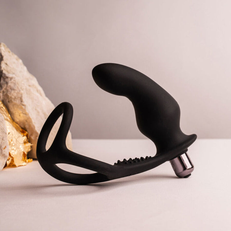 Ensemble plug anal et anneau pénien noir avec embout vibrant métallisé, posé près d'une pierre claire, tige courbe et anneau lisses sur fond neutre et sobre.