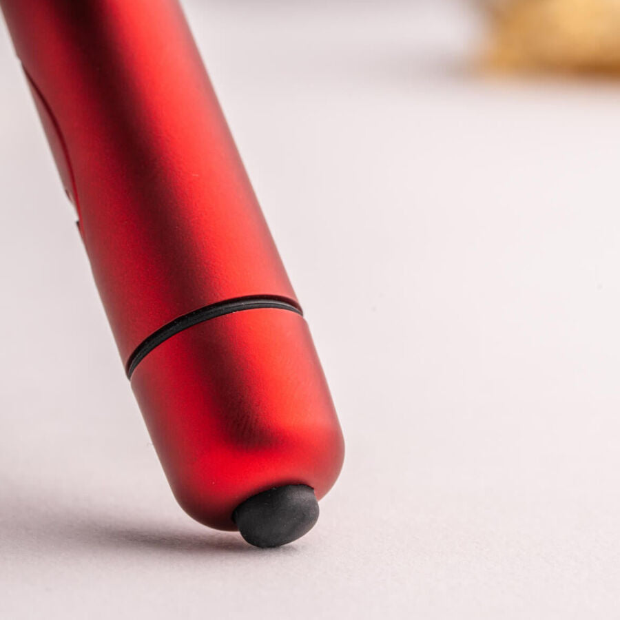 Gros plan de la base du bullet rouge montrant l'embout de commande noir et l'anneau de jonction, corps métallisé lisse couché sur surface claire et neutre.