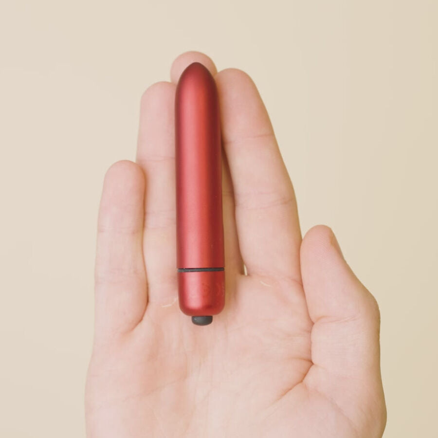Mini bullet rouge posé au creux d'une paume ouverte illustrant son format de poche, embout de commande visible, surface métallisée lisse sur fond neutre.