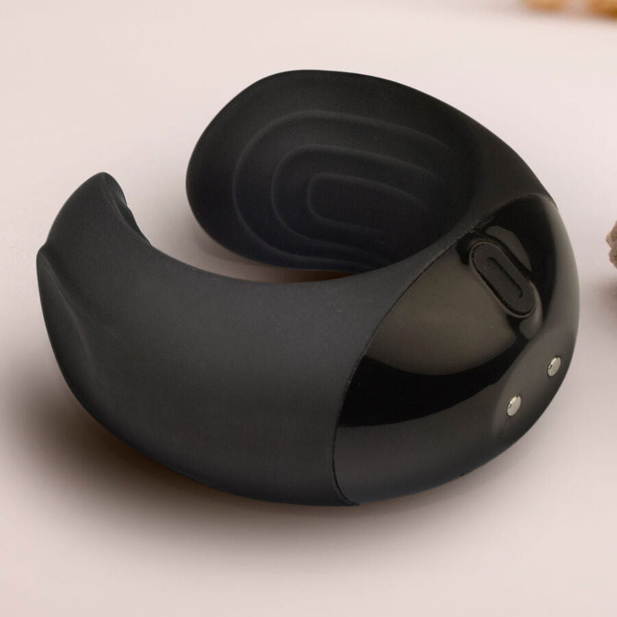 Vue de trois quarts de l'anneau pénien noir montrant le dos arrondi et la bullet logée, forme en croissant lisse posée sur fond beige neutre, sans aucun détail anatomique.
