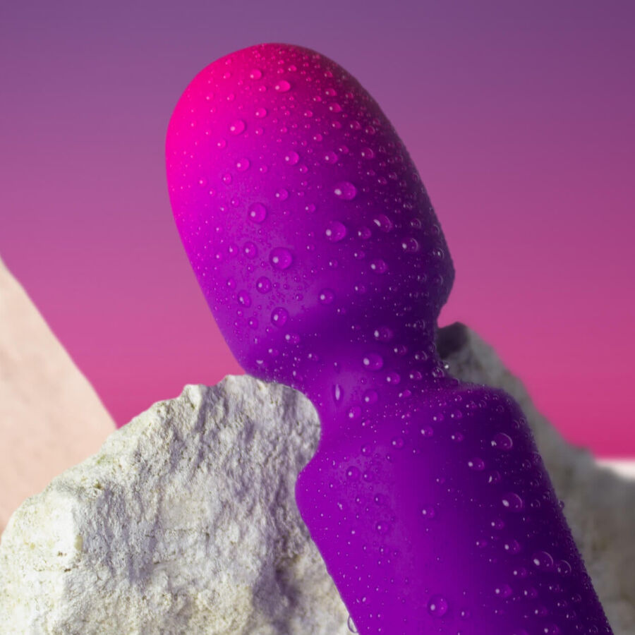Gros plan de la tête boule du mini wand rose-violet perlée de gouttes d'eau près d'une pierre, illustrant l'étanchéité du masseur en silicone non anatomique.