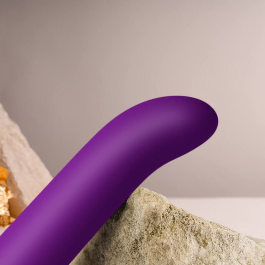 Gros plan de la tige incurvée du vibromasseur point G violet en silicone lisse posé contre une pierre, courbe profilée du stimulateur Chaiamo G étanche rechargeable.